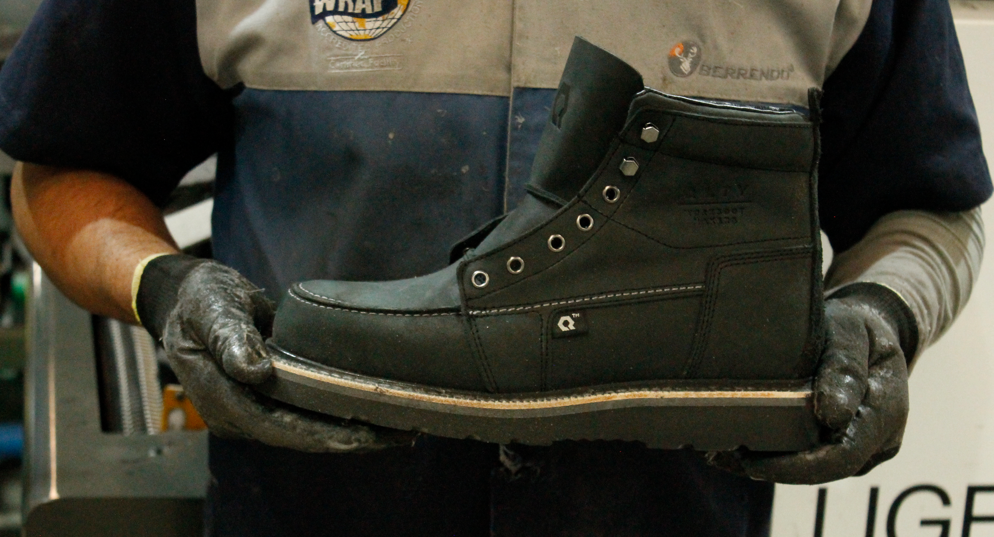 Man in gloves and work shirt holding a QLTY black steel toe work boot